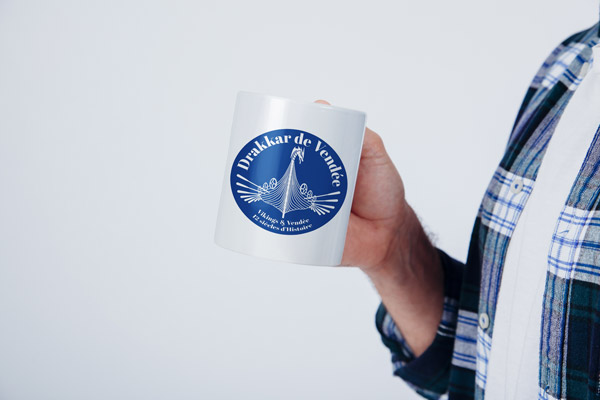 Main tenant un mug avec le logo de l'association du drakkar de Vendée.